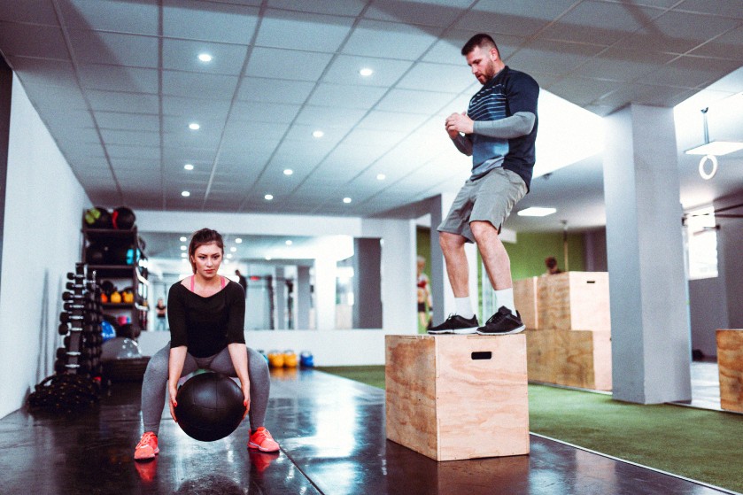 Na sali gimnastycznej trener personalny wydaje instrukcje młodej kobiecie, która ćwiczy na piłce