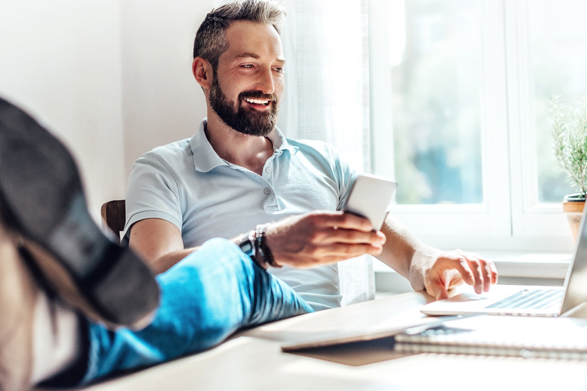 Wyluzowany mężczyzna z uśmiechem na twarzy pracuje na laptopie