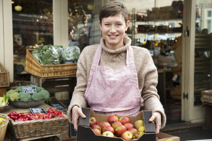 Sprzedawczyni na straganie trzyma pudełko z jabłkami