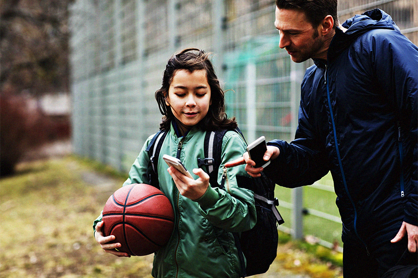 Tata z córką na boisku. Dziewczynka pokazuje tacie coś w telefonie
