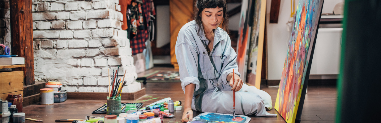 Artystka siedzi przed sztalugą i maluje obraz