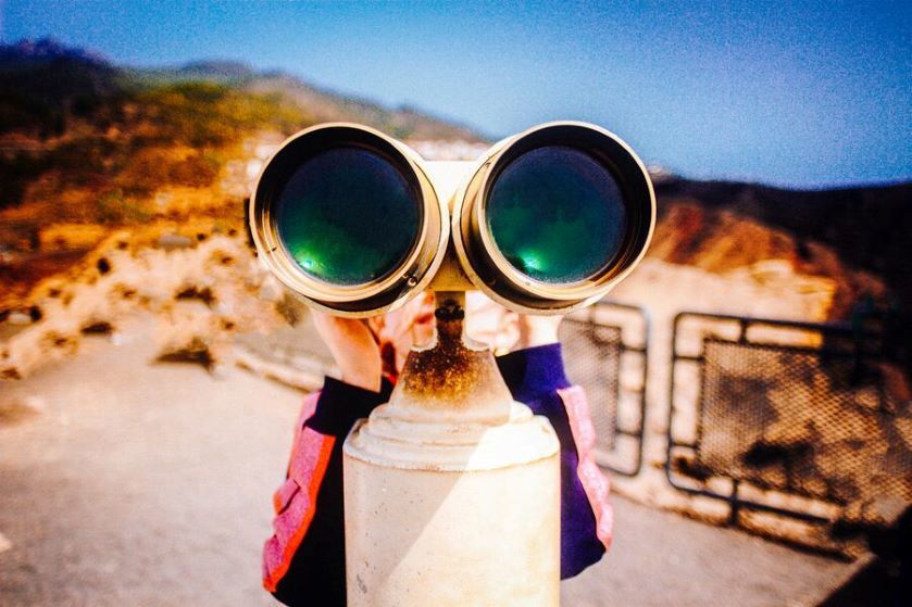 Zbliżenie na mężczyznę, który spogląda w dal przez wielką lornetę