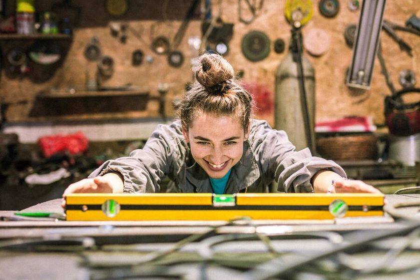 Uśmiechnięta młoda kobieta w warsztacie korzysta z poziomicy 