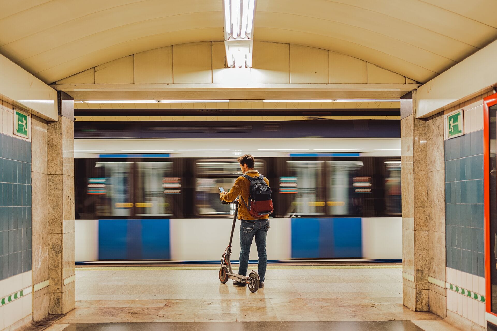 Osoba z hulajnogą na stacji metra korzystająca z płatności pay by link na smartfonie.