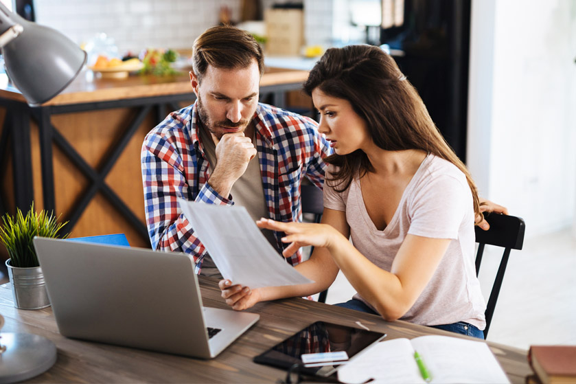 Kobieta i mężczyzna siedzą przed komputerem. Kobieta trzyma w ręku dokument - rozmawiają o nim