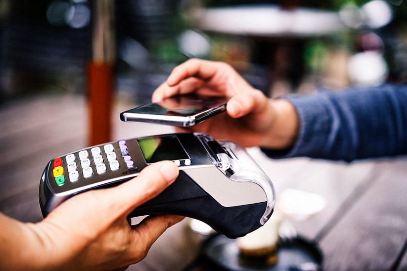 Płatność zbliżeniowa telefonem na terminalu POS - zbliżenie na ręce, które trzymaja urządzenia