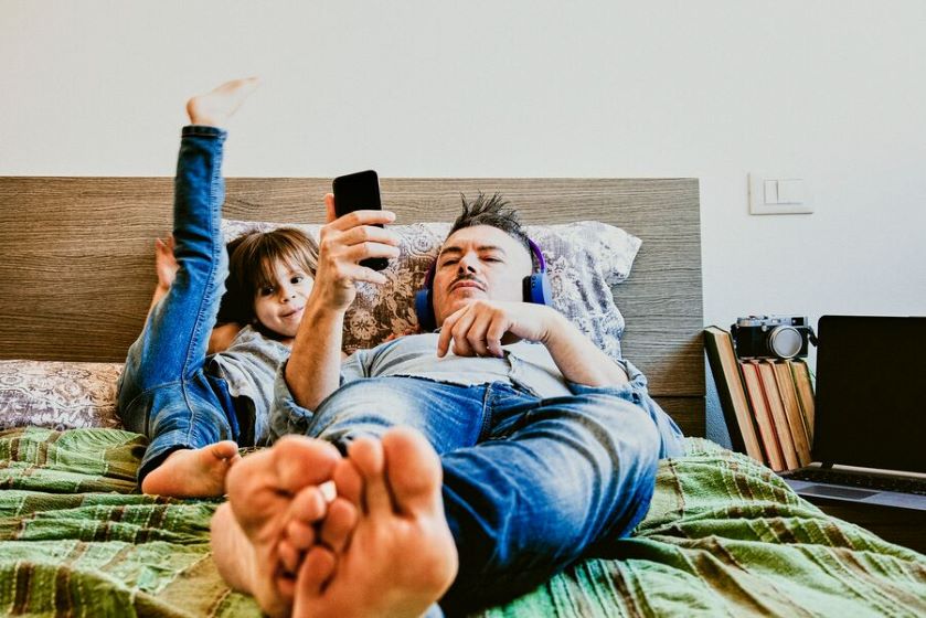 Ojciec z synkiem słuchają leżą na łóżku i słuchają muzyki z serwisu online dzięki subskrypcji.