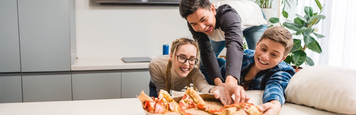 troje roześmianych nastolatków sięga po kawałki pizzy