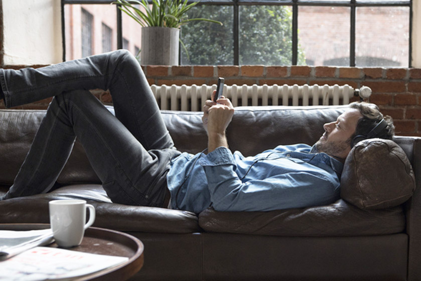 Mężczyzna leży na kanapie, słucha muzyki i korzysta ze smartfona