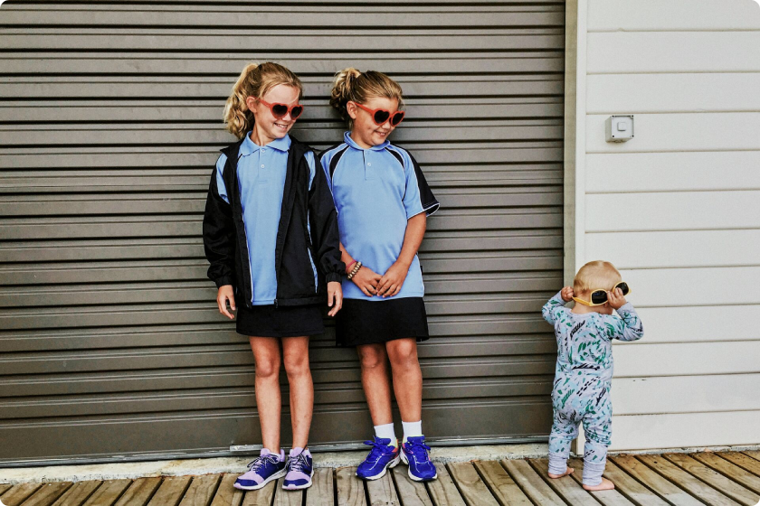 Dwie dziewczynki w okularach przeciwsłonecznych. Z uśmiechem obserwują pierwsze kroki bobasa