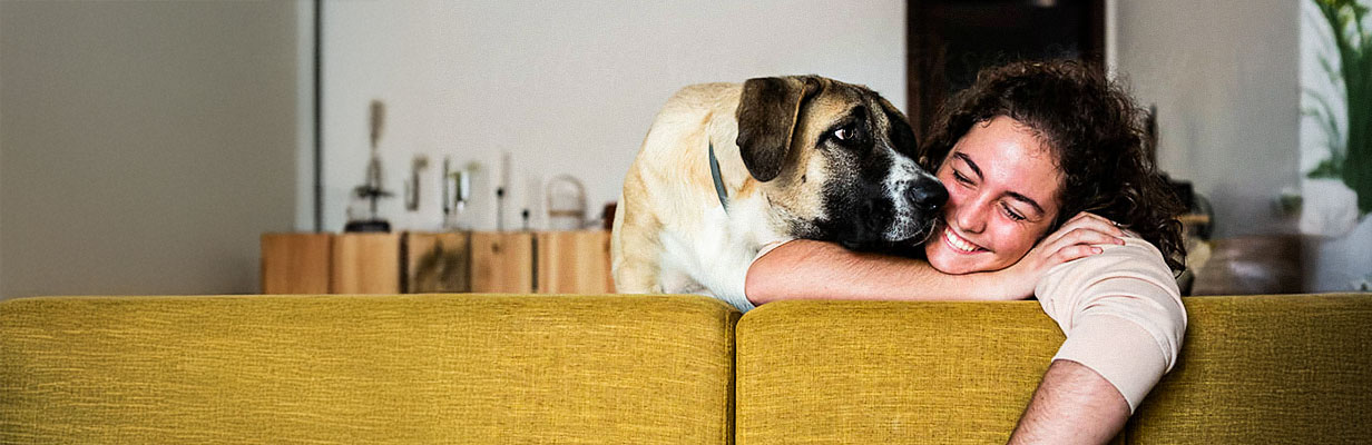 Uśmiechnięta kobieta w średnim wieku i pies siedzą na kanapie w swoim nowym mieszkaniu.