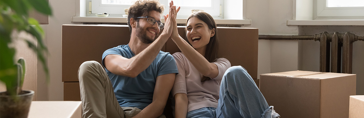 Młodzi ludzie siedzą na podłodze w mieszkaniu, uśmiechają się i przybijają sobie piątkę.