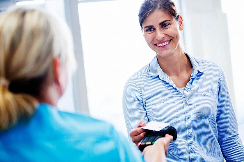 Uśmiechnięta kobieta płaci kartą zbliżeniowo na terminalu płatniczym