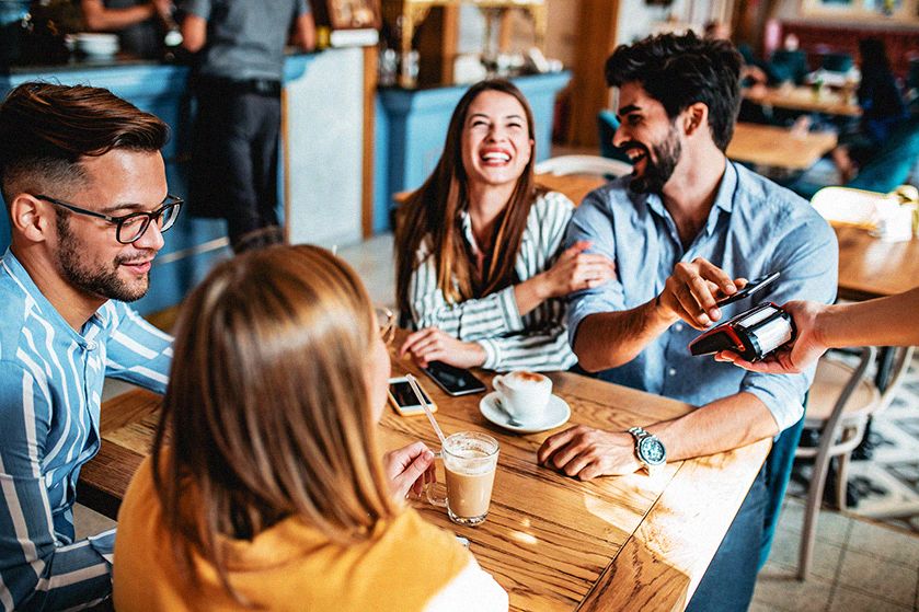 Dwie pary znajomych przy stoliku w kawiarni płacą telefonem za zamówienie