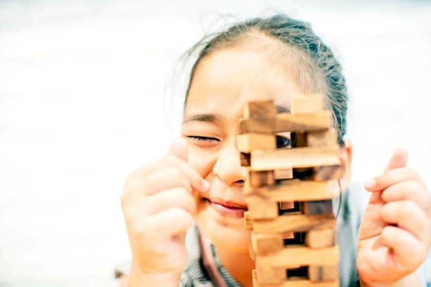 Dziewczynka spogląda przez okienko zbudowane z klocków gry Jenga