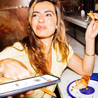 Młoda kobieta płaci kartą w kawiarni przykładając ją do telefonu z aplikacją eterminal