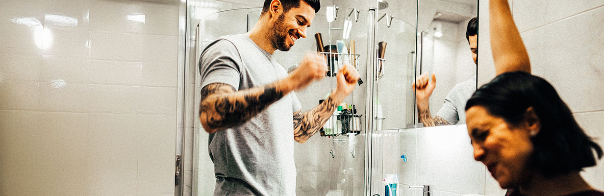 Szczęśliwa para w łazience, mężczyzna myje zęby, kobieta podnosi ręcę do góry z radości