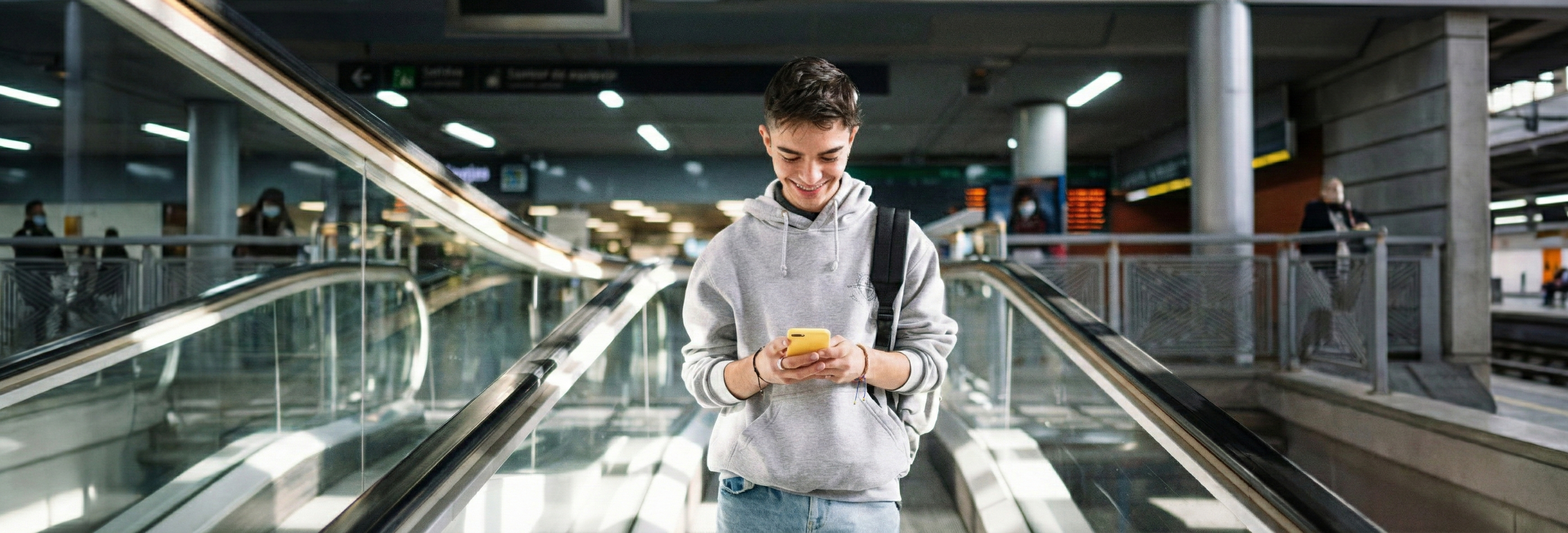 chłopak scrollujący telefon w przejściu w metrze