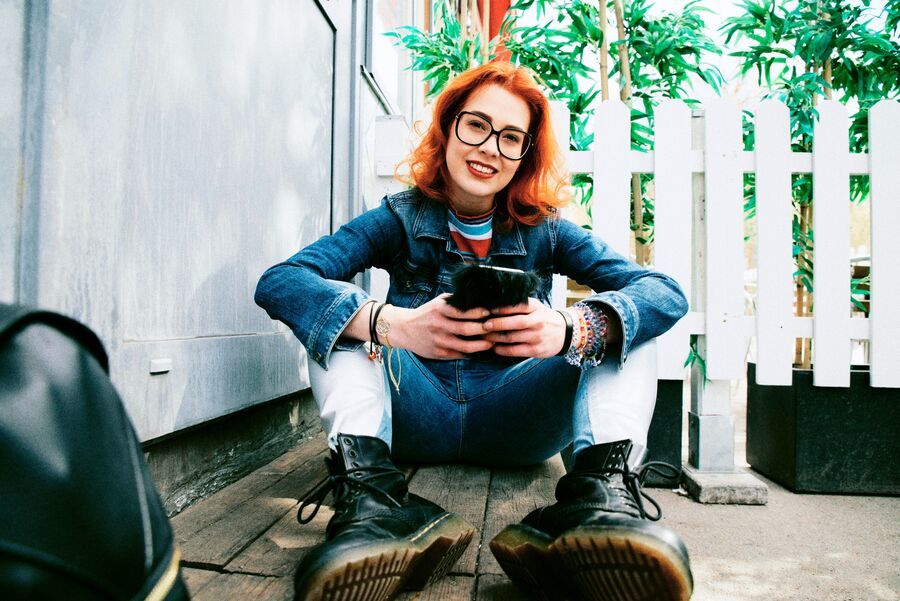 Rudowłosa dziewczyna siedzi na werandzie i korzysta z telefonu. 